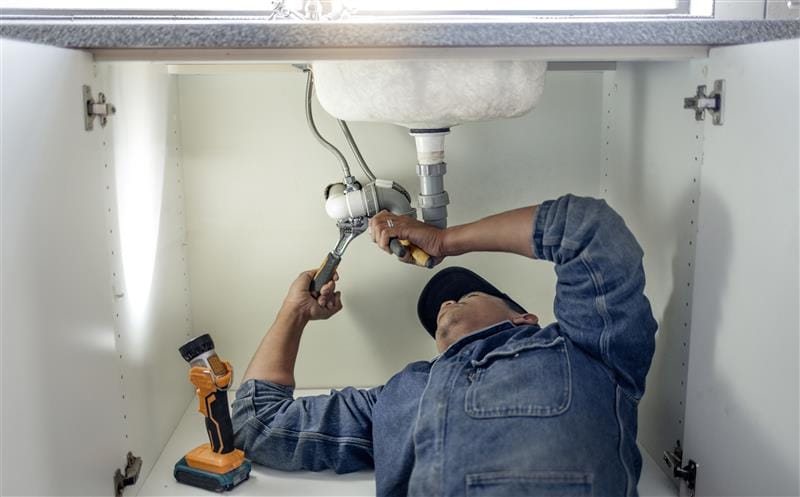 Plumber repairing pipes beneath a bathroom sink in West Linn
