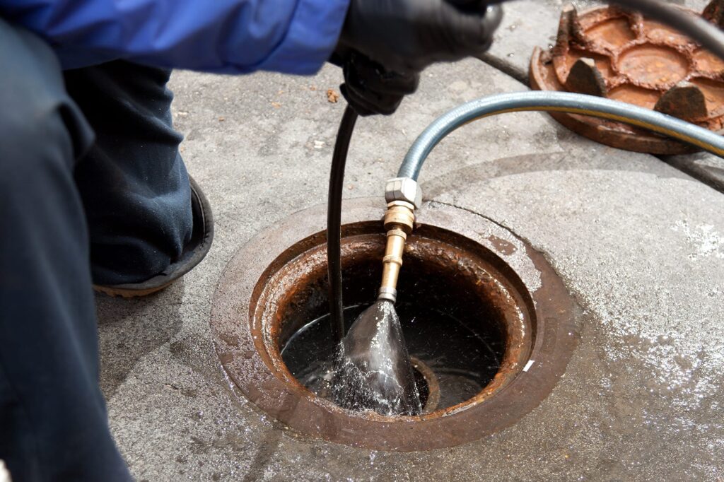 Plumber hydro jetting a sewer line through a manhole in West Linn