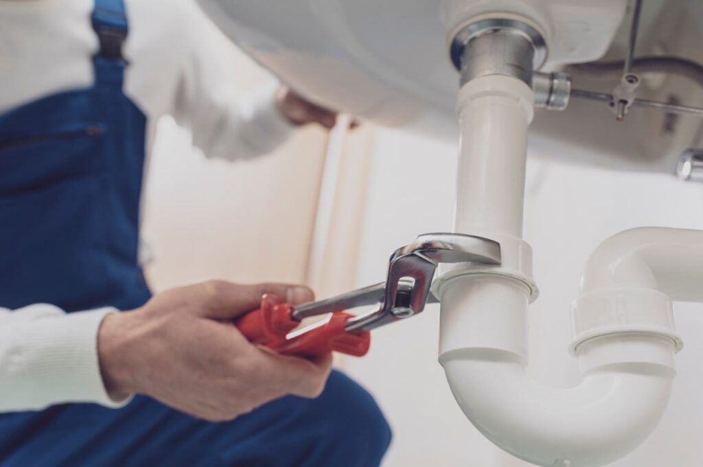 Plumber repairing a white drain pipe beneath a sink in West Linn