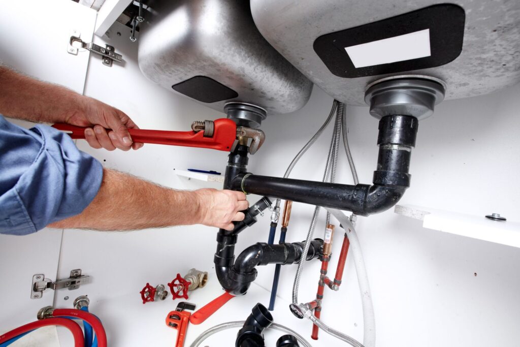 Plumber repairing drain pipes beneath a kitchen sink in West Linn